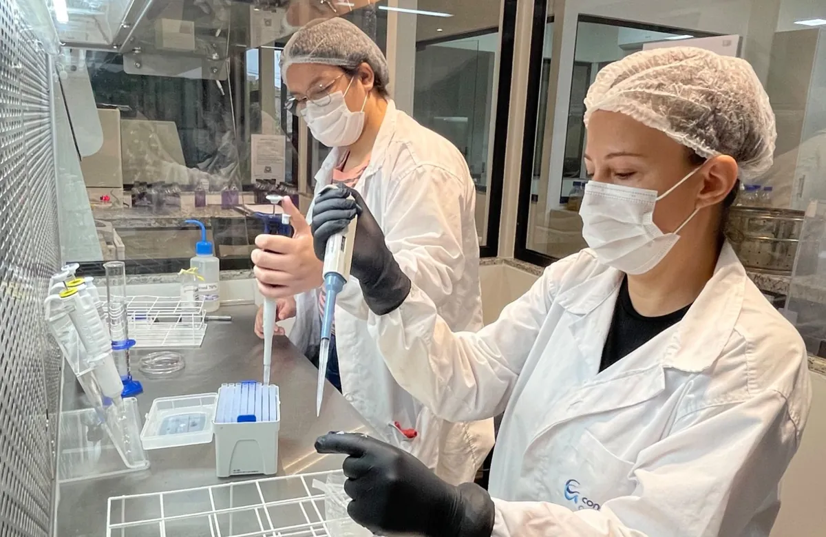 Analistas da Conágua Ambiental pipetando amostras em cabine de fluxo laminar, no laboratório de microbiologia